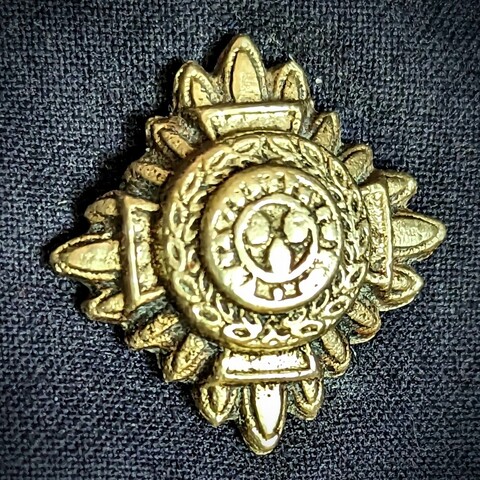 A vintage, polished brass Bath Star pip on a navy fabric background.