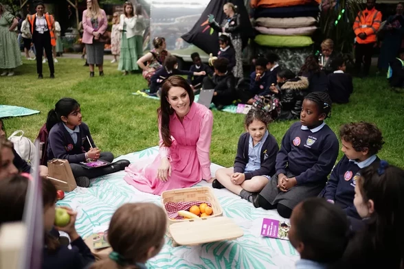 The princess of Wales is surrounded by children from many ethnicities. She looks weirdly out of place with a fake smile and the kid's faces express that they sense this too
