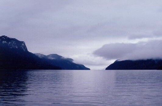 In the dark of evening, low clouds lie over the hills of a lake or a river.