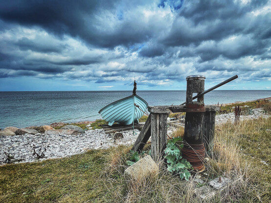 A lonely turquoise fishing boat lies on the pebble beach of Fornæs near Grenaa on the Baltic Sea coast in Denmark. 