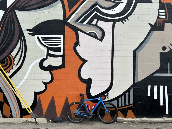 A blue gravel bike leaned against a mural of two faces