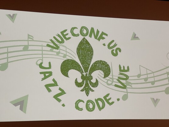 The Vueconf logo projected onto a screen. It’s a New Orleans Saints logo in green with the urls vueconf.com and jazz.code.vue 