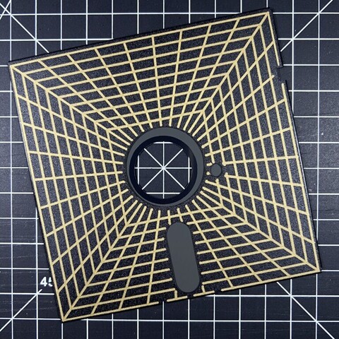A #PenPlot on top of a 5.25" black floppy disk of a vanishing point grid drawn in thick gold ink.