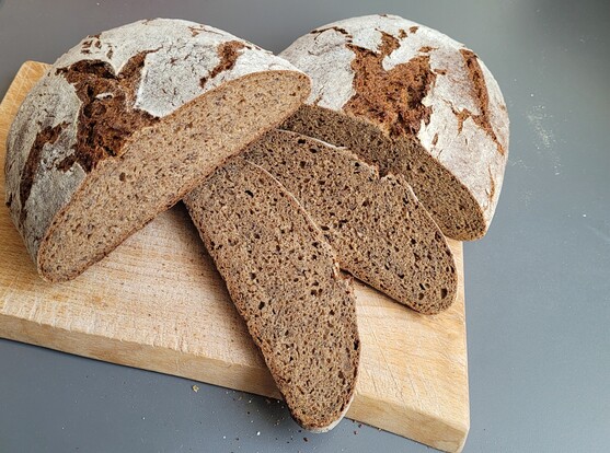 Derselbe Laib auf einem Schneidebrett, teilweise aufgeschnitten, so dass man die Krume sieht, mit Leinsaat drin. 