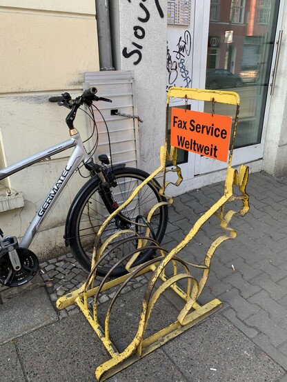 Gelber Fahrradständer in Form zweier Kängurus. Daran ein Schild: "Fax Service Weltweit"