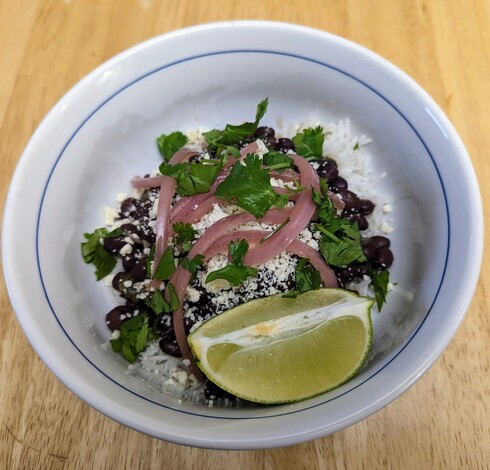 Cuban-style black beans on rice, topped with feta cheese, pickled red onion slices, coriander/cilantro, and a slice of lime.