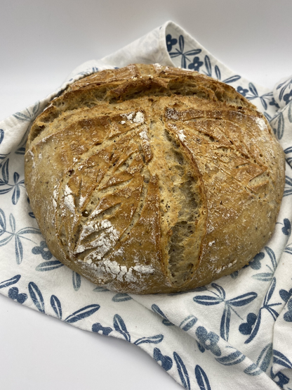 Multi grain sourdough loaf with leaf scoring on a blue and white tea towel 