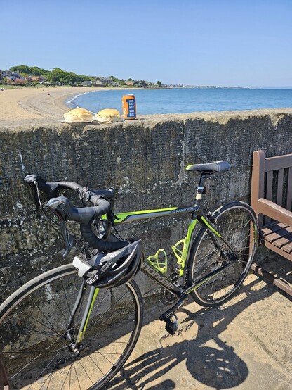 Picture of bike leaning against the harbour wall with a can of Irn Bru and two sausage rolls placed on top of the harbour wall