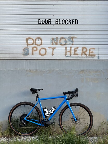 A blue Open UP leaned against a wall with the text “DOOR BLOCKED” and the test “DO NOT SPOT HERE” but it has been modified to say “DO POT HERE”