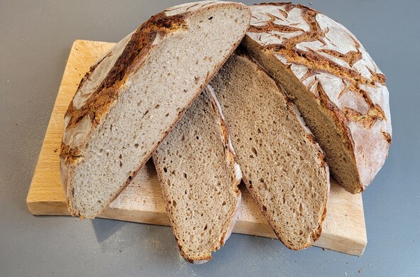 Das Krustenlaibbrot halbiert bzw. teilweise aufgeschnitten auf dem Schneidebrett. 