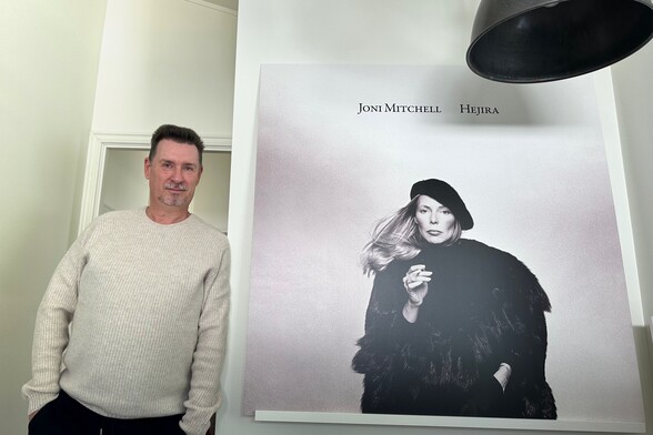 Photo of me standing next to the print of Joni Mitchell in my home office.
