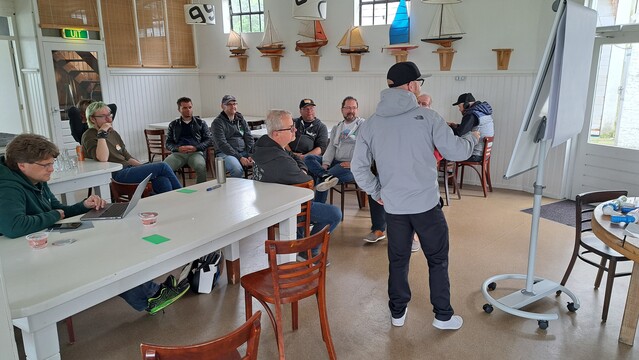 Ollie erklärt am Flipchart DDD Konzepte. Zuhörende sitzen in einem Stuhlkreis davor.