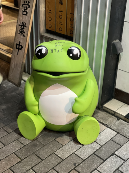 Cute large green frog figurine sitting on the street