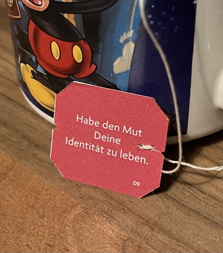 Ein rotes Schildchen von einem Teebeutel, worauf in weißer Schrift steht: „Habe den Mut Deine Identität zu leben.“