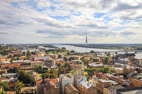 Old historic buildings in front of us. In the background a big river with several big bridges can be seen. A TV tower is near the river on the other side. Sky is blue and partly clouded.