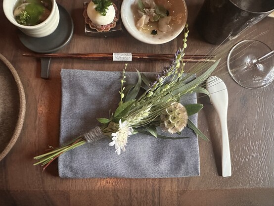 Seasonal herbs bound in thread sit atop a linen napkin, surrounded by small plates, chopsticks and a spoon.