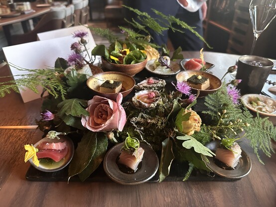 A square mound of flowers, ferns, and small plates filled with tiny artistic morsels