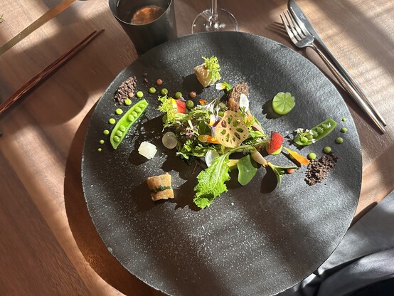 A round flat slate plate with green herbs and vegetables arranged in a minimalist style 