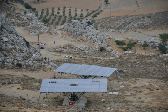 Zum besseren Verständnis der Größenordnung ein Foto mit zwei der Solaranlagen, einer Schafherde und einem Menschen mit blauer Jacke neben einem roten Auto weiter unten in dem abschüssigen Gelände. 