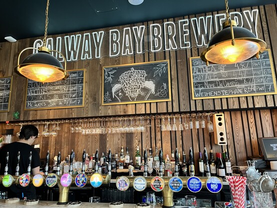 The bar and blackboard at The Beer Temple, showing the tap list and the Galway Bay Brewery branding behind hanging lights