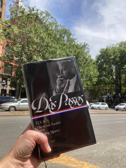Book cover with author photo and name “DosPassos” photographed in front of Seattle’s Pioneer Square