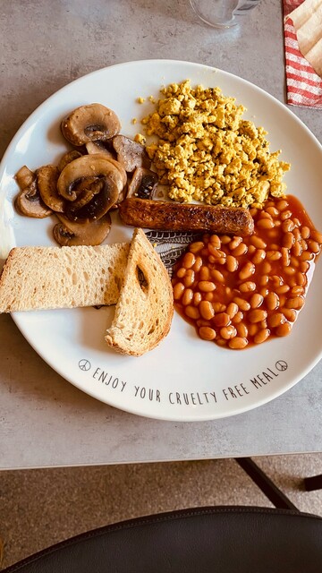 A filled plate with plantbased foods: white beans, toast, scrambled tofu, mushrooms and one vegan sausage.