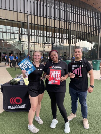 Three Headcount volunteers wearing Headcount T-shirts in front of the Moody Center in Austin