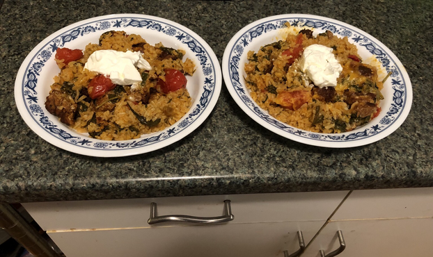 Plated dish. Mix of rice, tomatillo-poblano sauce, spinach, grape tomatoes, golden raisins, and chorizo, topped with melted cheese and a dollop of sour cream.
