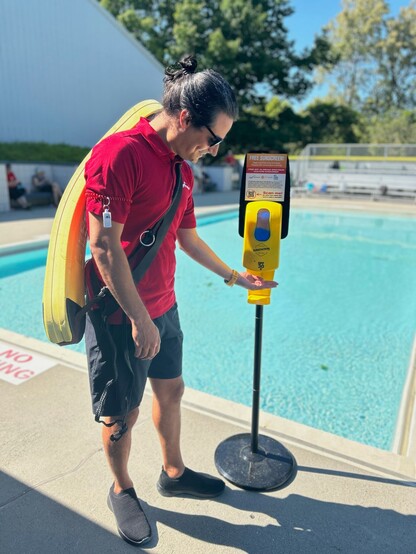 Lifeguard using the free sunscreen dispenser at the Steveston Community Pool.