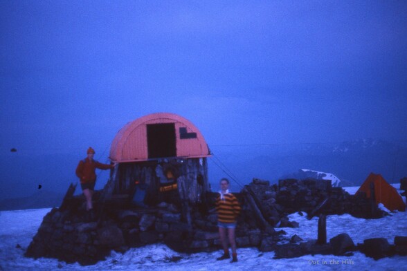 Myself and another stood in the twilight next to the summit shelter on Ben Nevis. Snow on the ground, and a small tent at the back.