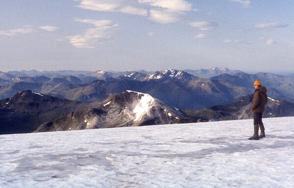 Morning. A young man stood on a snow covered hill top, looking at the view which contains several rows of ridges into the distance.