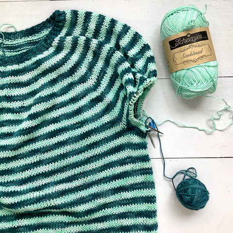 Flat lay view of the yoke and armhole of a striped circular yoke garment in teal and light turquoise. The armhole stitches are placed on a small circular knitting needle.