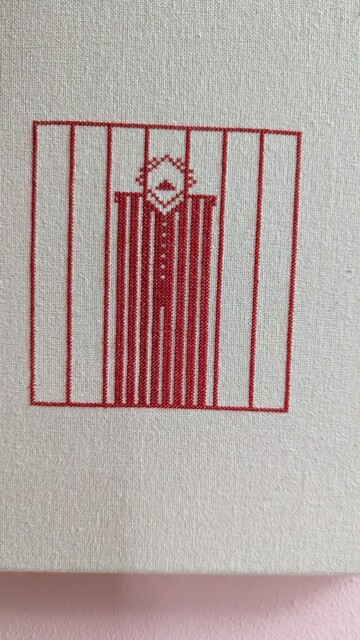  Stickereie, rot auf weiß. Ein Mensch hinter Gittern.