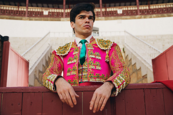 London-based photographer Owen Harvey delves into the rifts surrounding Spanish bullfighting in The Matador. In this image, a torero standing just outside the wood fence of a bullfight arena, with his arms laying on the fence and dressed with torero's dress, in strong pink and gold, and turquoise tie.