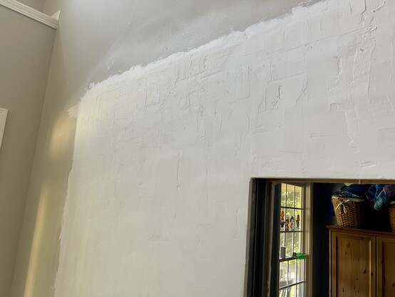 A section of a wall where large portions of drywall have been replaced, and mudding (joint compound) has been applied over it. The texture is bumpy and uneven, because it was applied very thickly to compensate for uneven joining of the old and new drywall surfaces. 