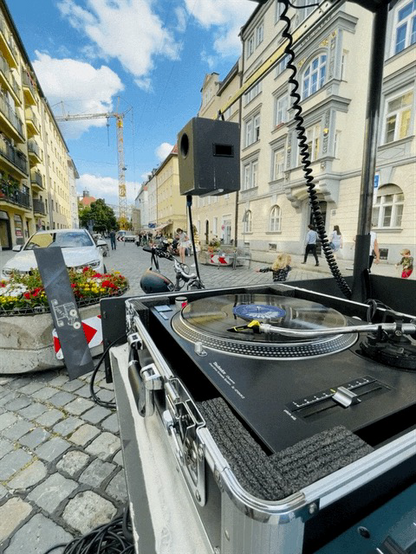 Straßenraum mit Menschen und im Vordergrund Plattenspieler. 