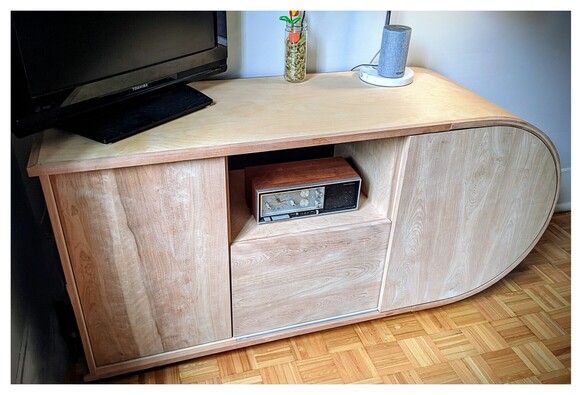 A recumbent U-shaped TV cabinet, seen from the front, made from plywood panels with cherry veneer and solid cherry wood shelves, doors and drawer fronts.