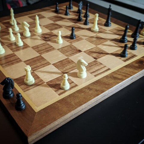 A chessboard made from several types of wood, with plastic playing pieces to simulate a court game.