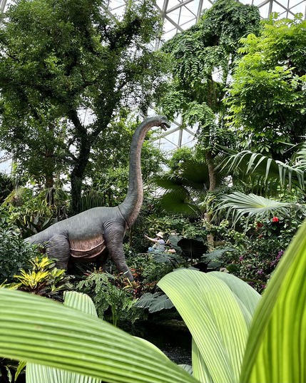 Large sculpture of a dinosaur amid tropical plants 