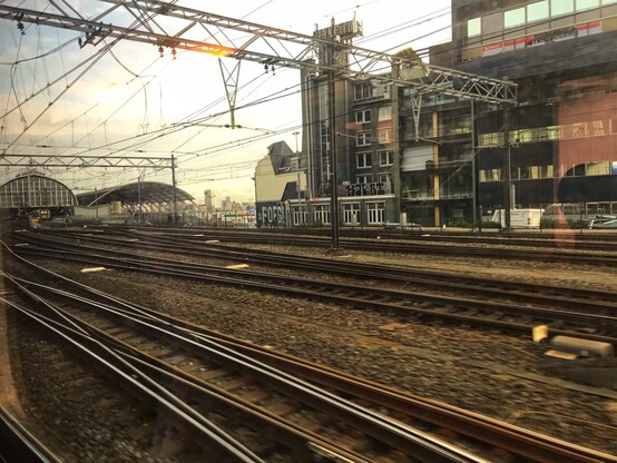 view from a train window: train tracks, many train tracks, a historical train station in the background from where the train just left