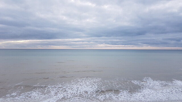 Looking out to sea in the English Channel. Heavy cloud, a grey horizon, and the white streaks of a wave going back out.