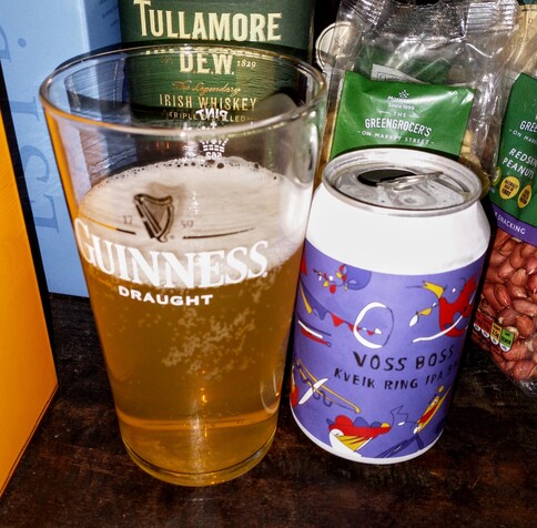 A Guinness glass to the left with the Guinness and harp logo, and to the right the empty can of IPA with a fancy design by a German artist.