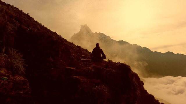 Silhouette of person sitting on the side of a mountain.
