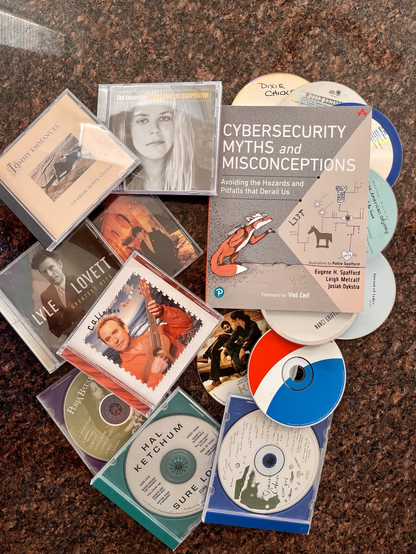 The book “Cybersecurity Myths and Misconceptions: Avoiding the Hazards and Pitfalls that Derail Us” surrounded by CD’s including Lyle Lovett, Colin Hay, Nanci Griffith, and Robbie Robertson.