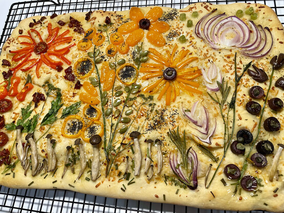 Another view of the cooked focaccia, as described. A red onion flower and kalamata olives are the flowers growing on the left. 