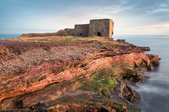 In this captivating photograph, the viewer is transported to Boddin Point in Angus, Scotland, UK. The remains of 18th-century lime kilns stand tall, bearing witness to the passage of time. Bathed in the gentle light of a light cloudy day, the sun's rays delicately caress the side of the lime kiln, illuminating its weathered surface. The kiln's boxy shape exudes an air of antiquity and decay, standing as a poignant relic of a bygone era. The long exposure captures the essence of stillness, inviting contemplation of the rich history that echoes within these time-worn walls.