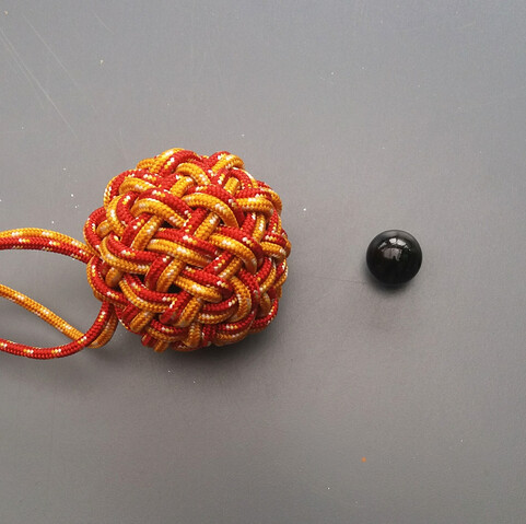 Pomme (nouage en forme de boule) à quatre-vingt quatre faces.
Le fil passe alternativement dessus-dessous.
Le nœud est doublé : un premier passage est réalisé avec de la cordelette jaune, le second avec de la cordelette rouge.
