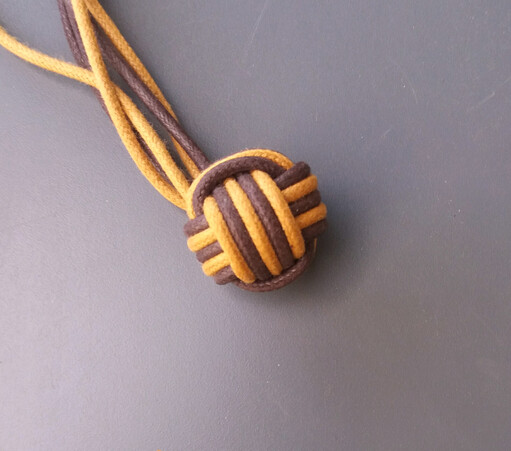 Une pomme de touline, nœud en forme de boule à six faces.
Chaque fil passe alternativement dessus-dessous.
Ici, le nœud est à cinq spires : chaque passage est effectué cinq fois.
De plus, le nœud est bicolore : un fil presque noir, un autre fil de couleur crème.
À chaque fois, les spires se succèdent alternativement au niveau de la couleur : une de couleur foncée, une de couleur claire, etc.