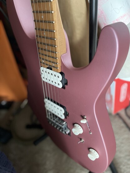 A close up of my new guitar, Nimona! A Charvel DK Mod24 Dinky style s-type electric guitar. She has white Seymour Duncan humbuckers, two white control dials, a 5 way pick up switch, and a series/parallel switch. Her color is satin burgundy mist. A beautiful color in between pink and purple, like a rose dark pink petal.