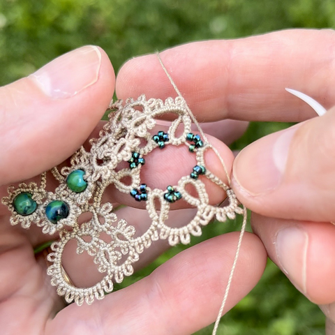 Tatting a lace necklace with ecru thread and green beads.